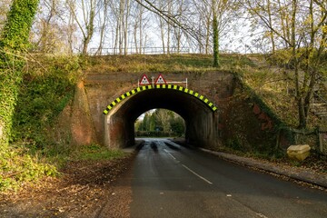 Low bridge warning signs over narrow road tunnel in autumn