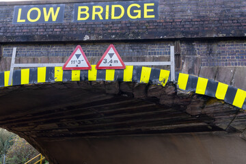 Low bridge warning sign showing height restriction and damaged brickwork