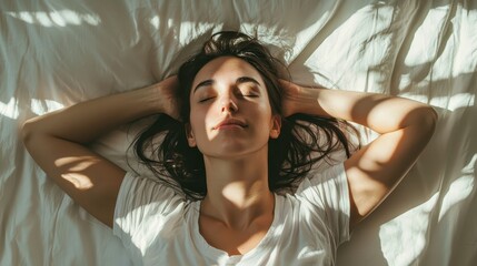 Fototapeta premium A serene woman lies on a bed, basking in sunlight, with her hands behind her head, exuding calm and tranquility.