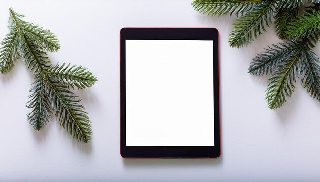 A black tablet with blank copy text screen and Christmas tree branches on white background	