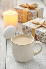 Fototapeta premium Warm and inviting, this features creamy beverage in ceramic mug, surrounded by beautifully wrapped gifts and glowing candle, perfect for cozy holiday atmosphere