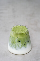 A glass of iced matcha green tea with milk on gray background. Antioxidant drink made of ground powder of green tea leaves.