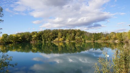 Obraz premium lake in autumn sun shines through the trees reflection of clouds in the water 