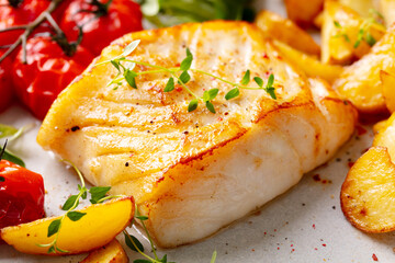 Roasted cod, codfish with baked potatoes and cherry tomatoes. Close up.