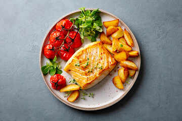 Roasted cod, codfish with baked potatoes and cherry tomatoes on plate. Grey background. Close up....