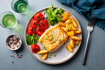 Roasted cod, codfish with baked potatoes and cherry tomatoes on plate. Grey background. Top view.