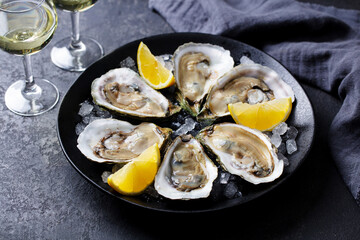 Fresh oysters with lemon on a plate and white wine in a glass. Grey background. Close up. © annapustynnikova