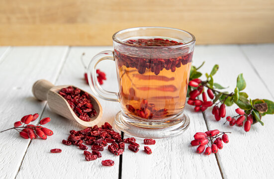 Berberis vulgaris also known as common barberry, European barberry or barberry tea drink in class mug in home kitchen. Dried and fresh berries for decoration on wooden board background.