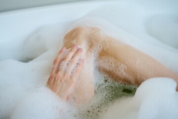 Fototapeta premium Medium close up of unrecognizable female body covered with white foam, woman resting in bathtub