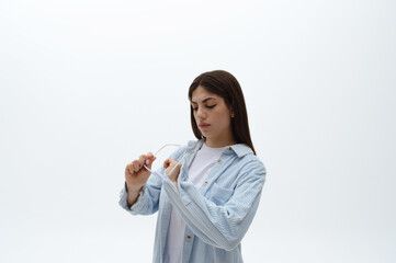 Portrait of a beautiful Eastern woman in a blue shirt cleaning her glasses isolated on white. Wipe the glasses. Copy space.