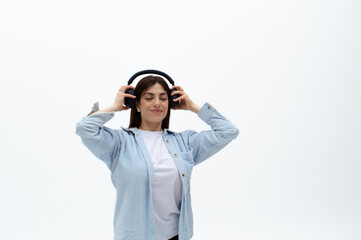 Cheerful young eastern woman in a blue shirt with headphones, keeping her hands on it, enjoying...