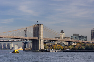 Obraz premium View of Brooklyn Bridge with ferry passing under clear sky.