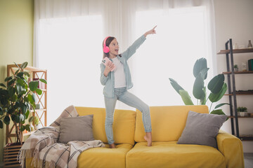 Joyful young girl with headphones enjoying music in a cozy living room, standing on a bright yellow...