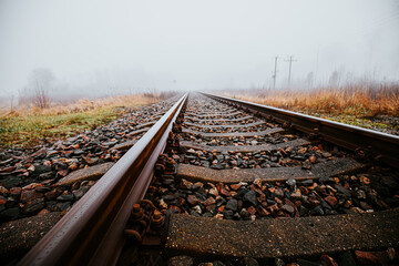 Straight railroad tracks surrounded by foggy fields and grass, leading into the horizon. The mist...