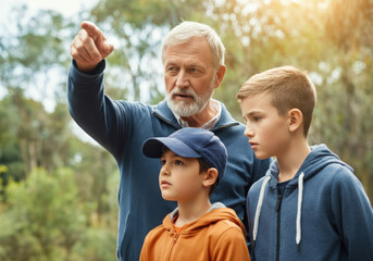 Fototapeta premium Senior man pointing his finger and showing something interesting to his two grandchildren during a walk in the forest
