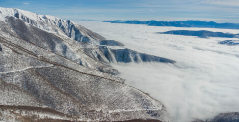 Aerial view of a snowy mountain range emerging above a thick layer of smog and fog, highlighting...