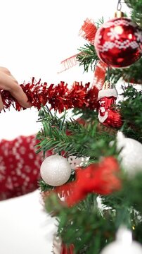 Vertical Merry christmas and happy holidays, hand of an asian woman is decorating the spruce tree with a tinsel garland, indoors home at winter. Xmas ball hanging of fir branches for decoration