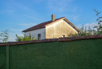 Casa r&uacute;stica sin pintar tras muro de jard&iacute;n