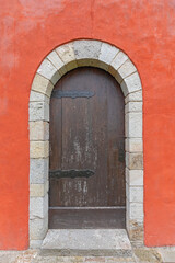 Closed Wooden Arch Door at Vivid Red Building Wall
