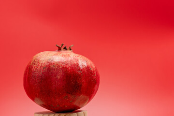 A ripe pomegranate sits on a wooden surface. The fruit is round and has a stalk on top. The image...