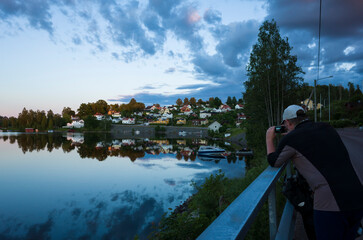 Bengtsfors city by the Lel&aring;ng lake at Swedish summer night, Man is photographing city view reflecting in calm water, Sweden