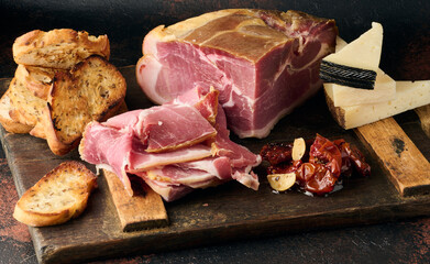 A piece of prosciutto, slices of ciabatta and cheese on a wooden board