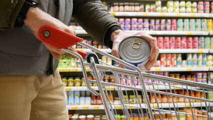 A customer putting a tin of canned food into a shopping trolley