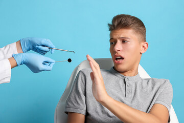 Dental phobia. Dentist working with scared man on light blue background, closeup