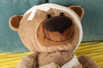 Cute teddy bear with bandages and adhesive medical plasters on bed