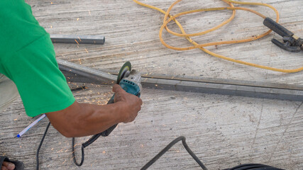 A worker hands are holding and using a tool to cut steel until it sparks in a construction site.
