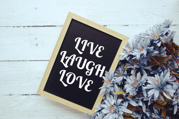 Live Laugh Love typography text written on wooden blackboard with flower bouquet decorate on wooden...