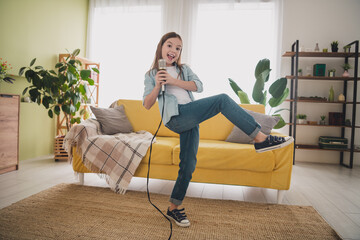 Fototapeta premium Adorable young girl singing joyfully into a microphone in her cozy living room surrounded by vibrant decor