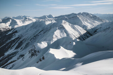 Snowy mountain peaks, rugged valleys stretch toward horizon under clear blue sky