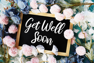 Get Well Soon written on chalkboard with flowers blooming top view on blue background