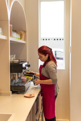 Redhead waitress wearing colorful apron red view in profile preparing a machine coffee in professional Italian coffee maker. in cafeteria bakery.