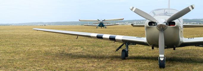 Biplane and small sport airplane with propeller, panoramic landscape with two aircraft on airfield.