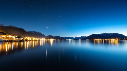 Nighttime view of a calm lake reflecting mountains and stars in a serene landscape