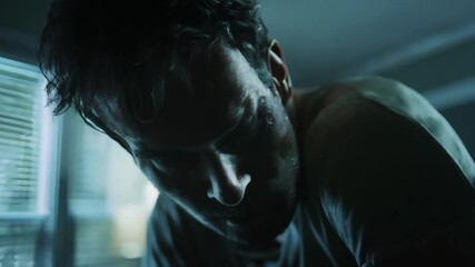 Intense closeup of menacing man in dim light. Sweat covered face with shadowy features suggests tension and aggression. Cinematic portrayal of threatening character