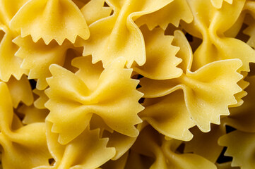 A close-up view of uncooked farfalle pasta, showcasing its distinctive bow-tie shape and golden...