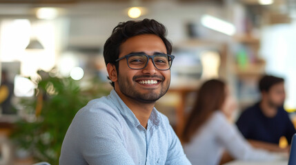 Obraz premium A smiling man at a cafe works on his laptop while friends engage in conversation nearby