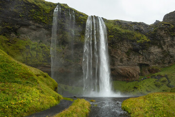 Obraz premium The beautiful Seljalandsfoss waterfall in South Iceland offers a unique perspective, with pathways allowing visitors to admire its beauty from behind the falls. Tourists enjoying Iceland.