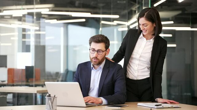 Young businesswoman sexually harasses a male coworker places hand on shoulder at workplace in business office. Beautiful female flirts with shocked worried businessman colleague who is sitting at desk