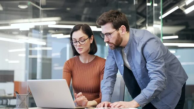 Boss consult young female worker at workplace in business office. Male manager advises, talking to an employee about a development project. Executive explains work issues using laptop computer