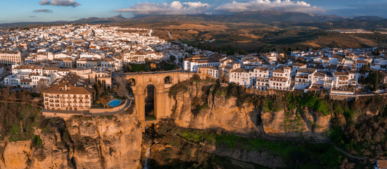 The image shows an aerial view of Ronda, Spain, highlighting the Puente Nuevo bridge over a deep gorge, with whitewashed buildings on cliff edges.