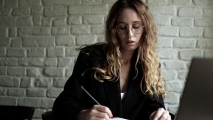 Woman Writing in a Notebook with Laptop Nearby