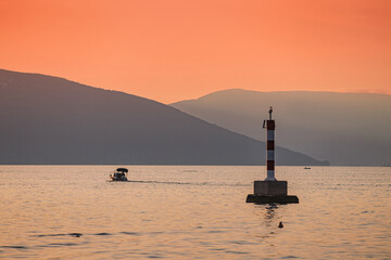 Fototapeta premium Small motorboat sailing near a cardinal mark at sunset with mountains in the background