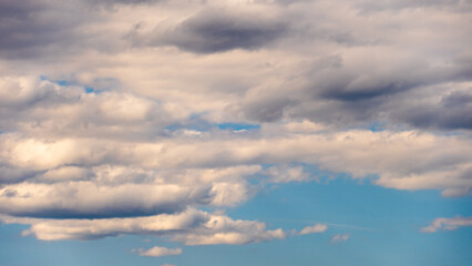 Fluffy orange clouds in a blue sky illuminated by the light of the setting sun. Pure nature, untouched by man. Climate change as a result of human activity.