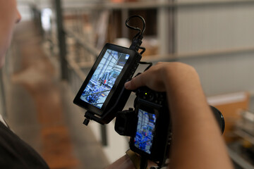 Manos de mujer joven cfilmando con máquina digital y monitor. Imagen horizontal, bokeh de fondo, lugar industrial