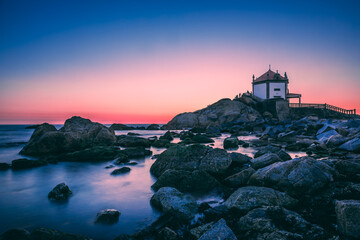 The senhor da pedra chapel stands on a rocky outcrop along the coast of vila nova de gaia, portugal, bathed in the warm glow of the setting sun, creating a serene and picturesque scene