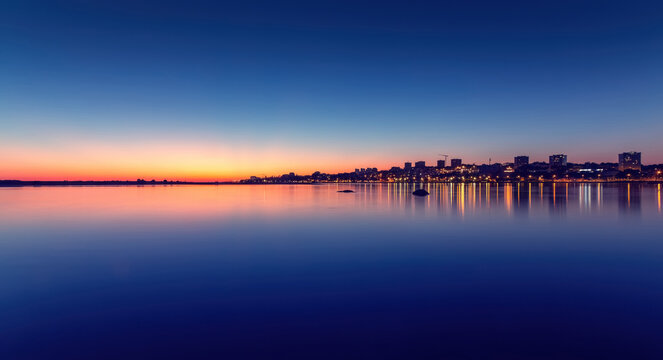 City lights reflecting on douro river at sunset with orange, pink, purple, and blue color gradient in the sky in vila nova de gaia, portugal observing Porto, Portugal